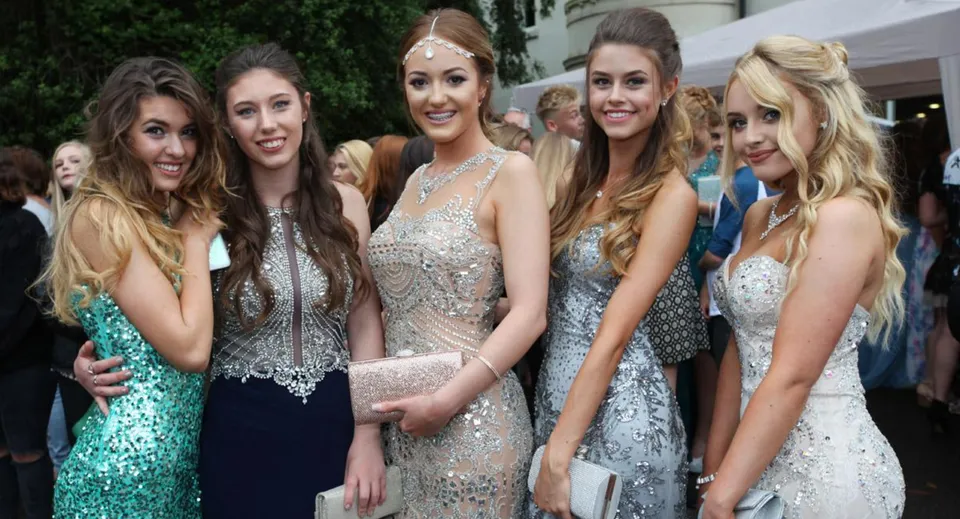 Un gruppo di giovani donne in abito formale in posa davanti ad edifici e aree verdi del campus della City of London Freemen’s School.