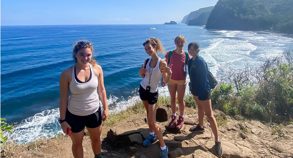 Studenti della Hawaii Preparatory Academy si trovano su una scogliera e guardano l'oceano blu e una costa montuosa.