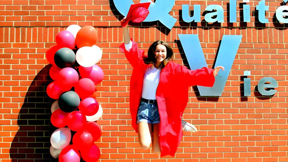 Una donna con un outfit rosso sta davanti a una parete di palloncini colorati alla École Aux quatre vents.
