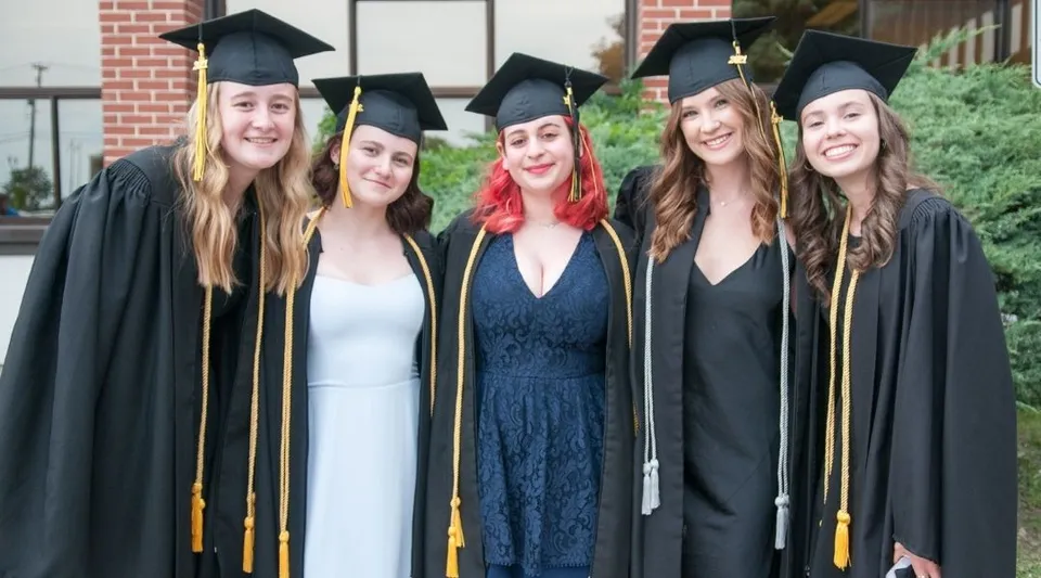 Cinque diplomate della John Rennie High School sono davanti a un edificio in mattoni e festeggiano il loro diploma.