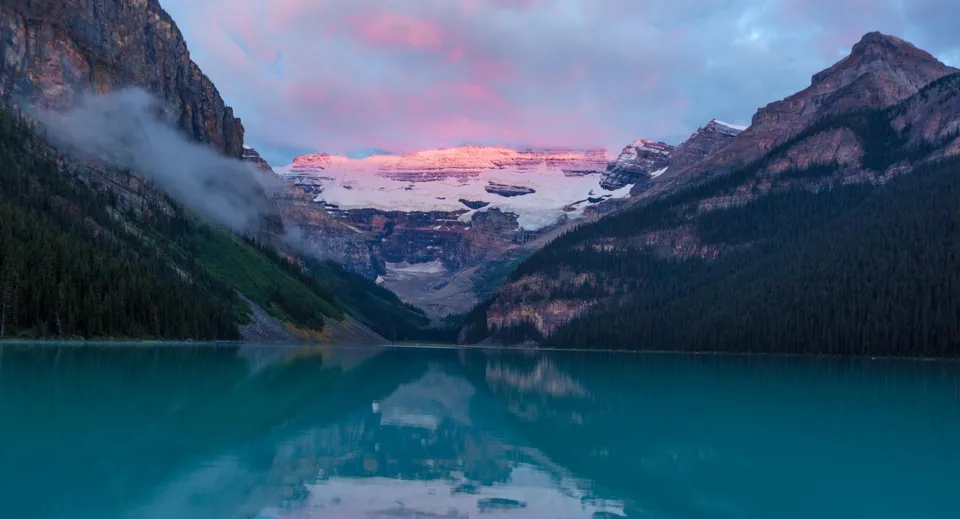 Un lago di montagna nelle Alpi riflette le cime innevate al tramonto.