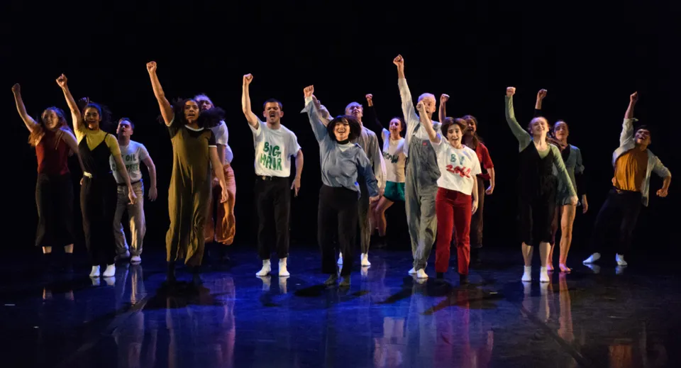 Studenti del St. Coleman's College sono su un palco con le braccia alzate ed eseguono una vivace performance.