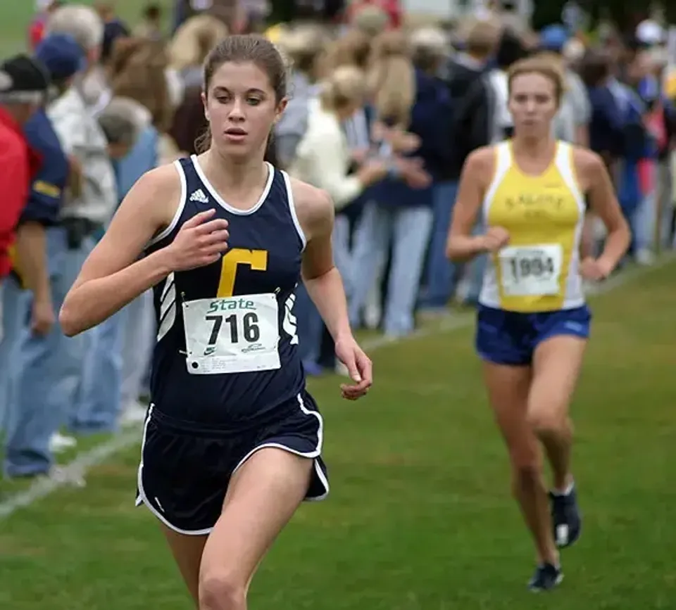 Un'atleta della Clarkston High School corre durante una gara di corsa campestre su un prato.