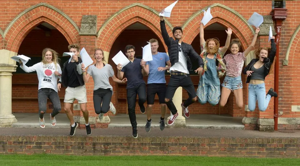 Un gruppo di studenti della St. John’s School a Leatherhead salta davanti a un edificio in mattoni con porte ad arco.