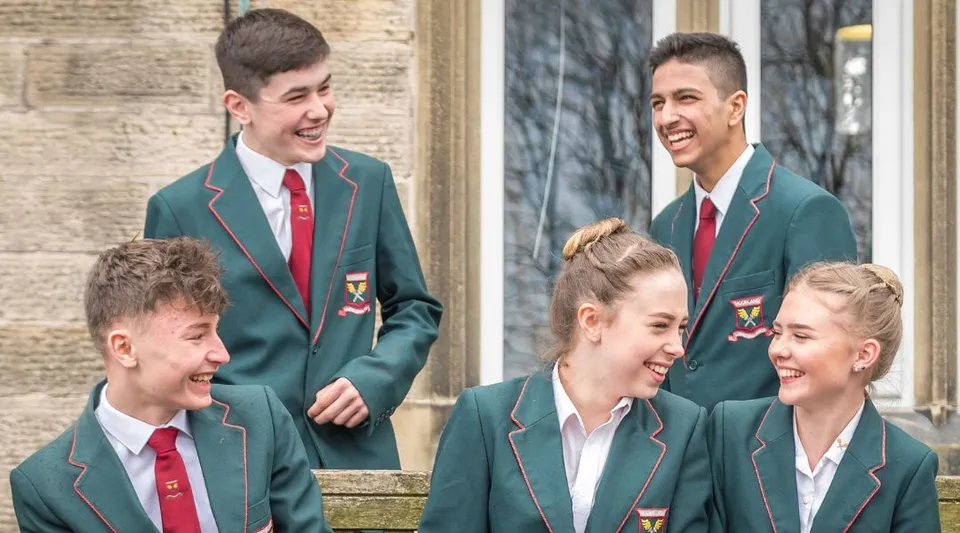 Un gruppo di studenti in uniforme scolastica chiacchiera davanti a un edificio in mattoni nel campus della Moorland School.