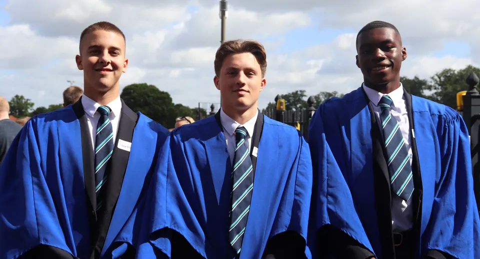 Tre studenti della Brentwood School in toga blu da diploma sono in piedi davanti a un cielo nuvoloso con alberi sullo sfondo.