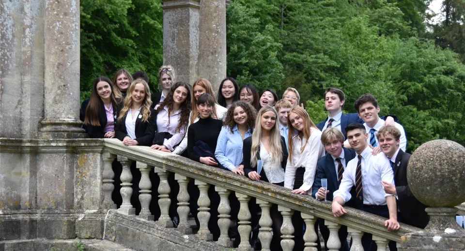 Un gruppo di studenti si trova sul balcone del Worksop College circondato da vegetazione verde e colonne in pietra.