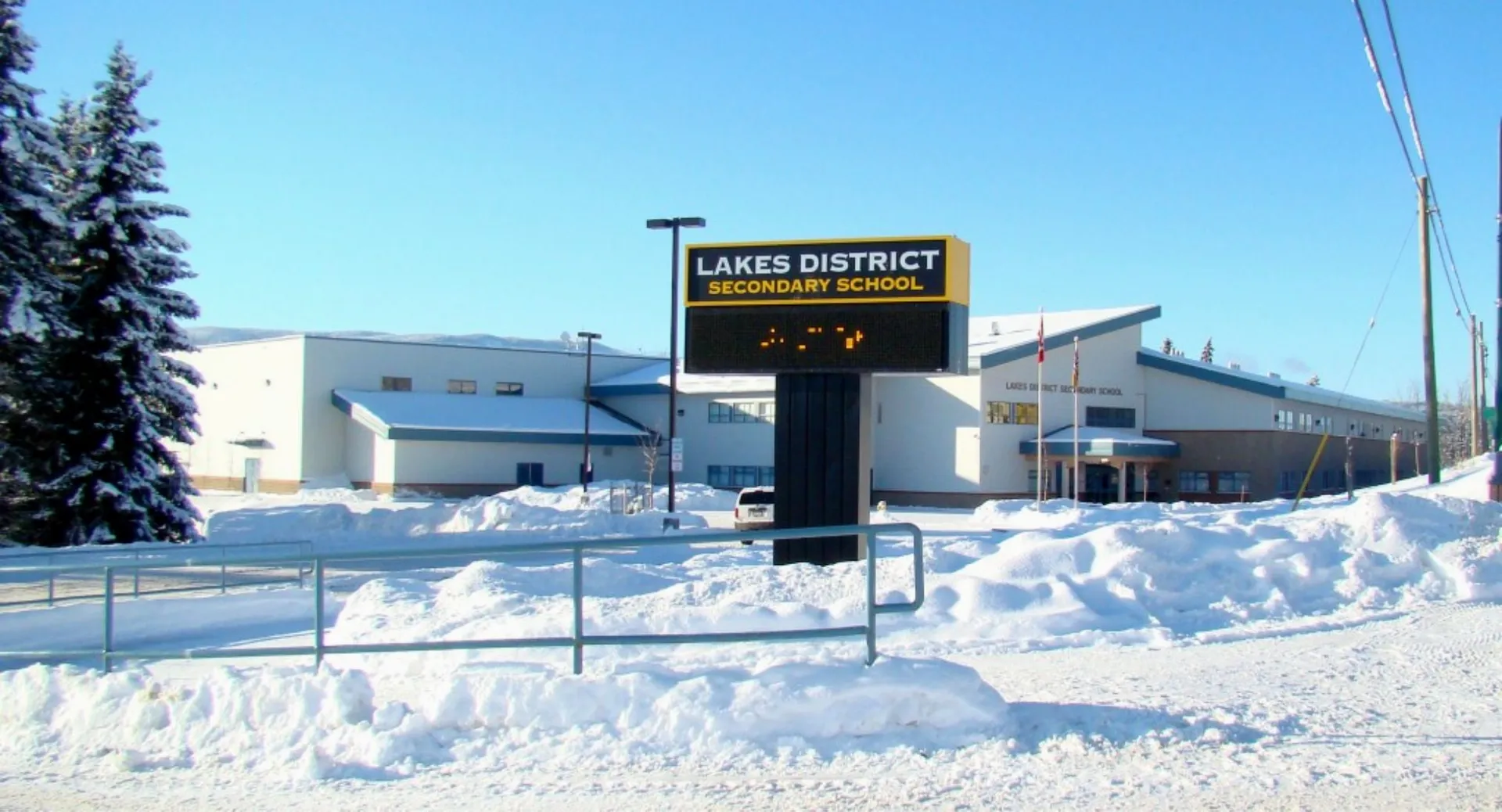 Il campus innevato della Lakes District Secondary School mostra un grande cartello davanti a un cielo blu.