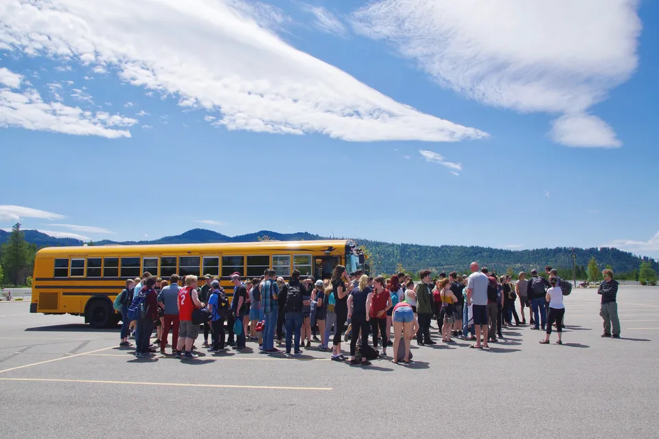Gli studenti della Mount Baker Secondary School si trovano davanti a uno scuolabus giallo con montagne e cielo blu sullo sfondo.