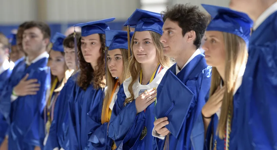 Un gruppo di diplomati in toghe blu in posa per la foto di diploma della Newman Central Catholic High School.