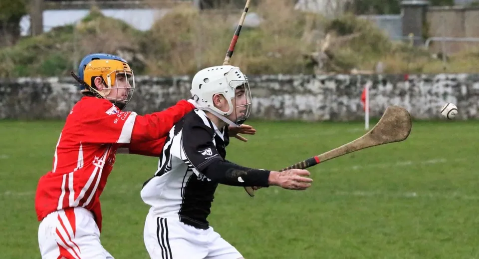 Due giocatori in abbigliamento sportivo giocano sul campo sportivo del St. Cuan’s College con un edificio sullo sfondo.