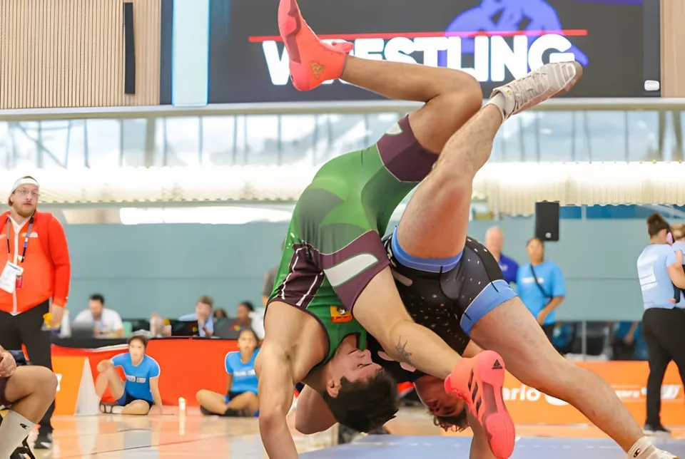 Una lottatrice con una divisa rossa e verde esegue una mossa acrobatica sul tappeto durante una competizione della École secondaire Népisiguit.
