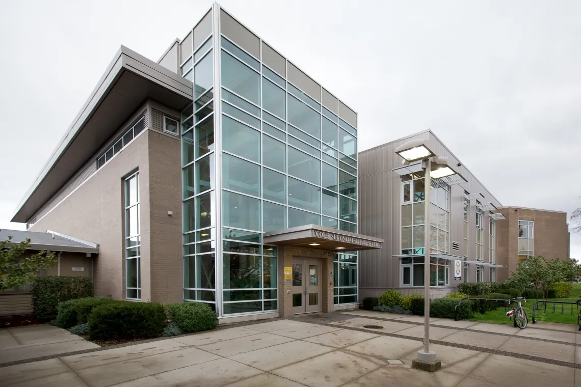 El moderno edificio de varios pisos con fachada de cristal de la Jules Verne School Vancouver está rodeado por un camino pavimentado y zonas verdes.