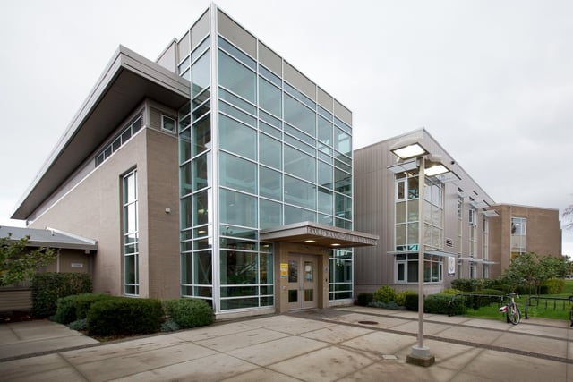 El moderno edificio de varios pisos con fachada de cristal de la Jules Verne School Vancouver está rodeado por un camino pavimentado y zonas verdes.