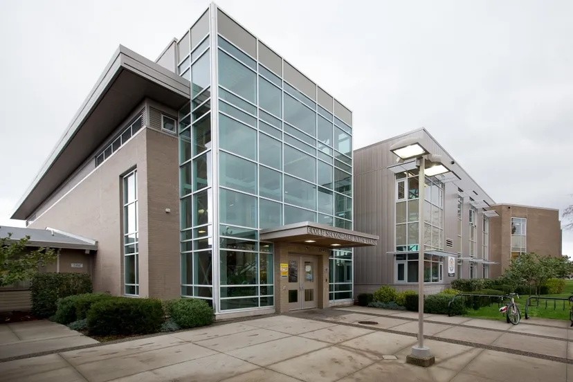 Il moderno edificio a più piani con facciata in vetro della Jules Verne School Vancouver è circondato da un vialetto pavimentato e aree verdi.