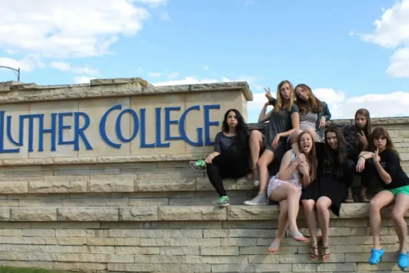 Grupo de chicas sentadas en un muro de piedra con el cartel de Luther College