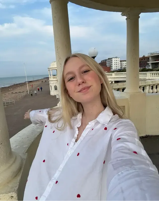 Studentessa bionda si scatta un selfie su un lungomare con colonnato e spiaggia