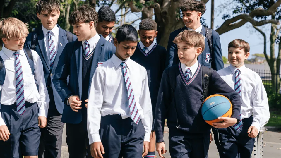 Un gruppo di studenti e studentesse del Sacred Heart College in divisa scolastica si trova all'aperto davanti ad alberi ed edifici.