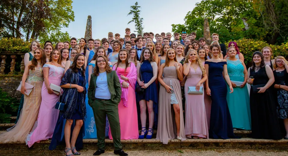 Un gruppo di giovani donne in abiti eleganti posa insieme davanti a un paesaggio nel campus della Claremont School.