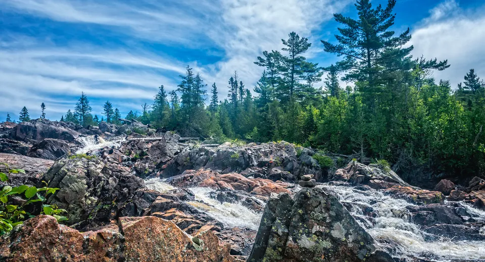Un paesaggio roccioso con una cascata e alberi sempreverdi sotto un cielo blu vicino alla Ridgetown District High School.