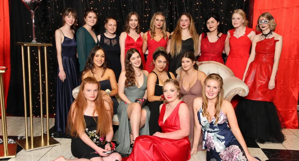 Un gruppo di studentesse del Paraparaumu College in pose con abiti eleganti davanti a uno sfondo scuro con luci scintillanti.