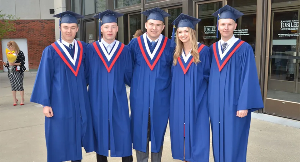 Cinque studenti della Grant Park High School indossano abiti da diploma blu davanti a un edificio scolastico.