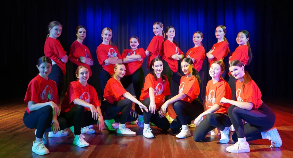 Un gruppo di giovani studentesse siede sul palco della Benowa State High School davanti a un sipario blu.