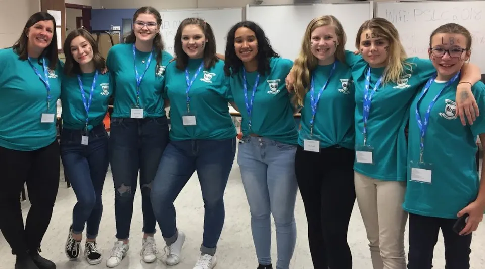 Un gruppo di studentesse con magliette verdi si trova insieme in un edificio scolastico della Leo Burke Academy.