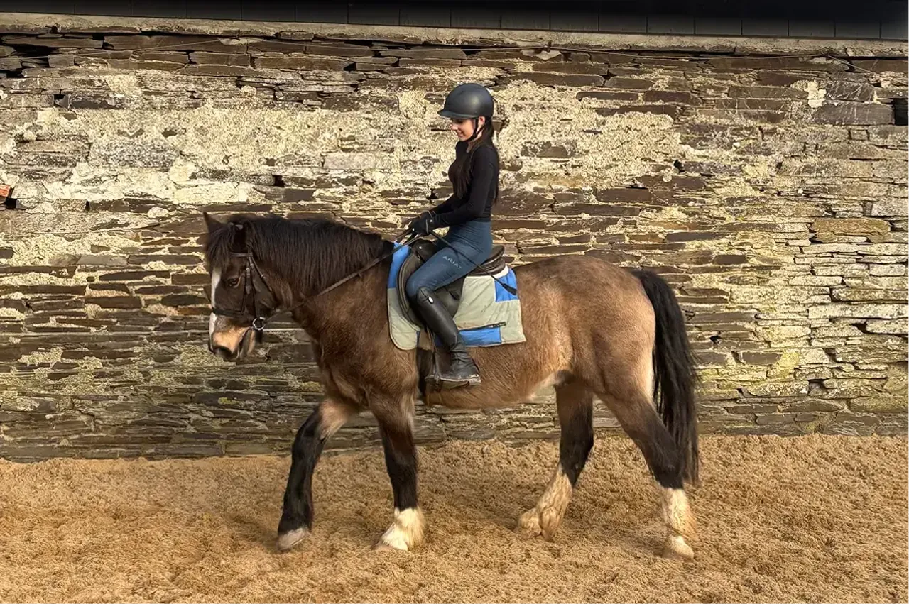Ragazza con casco cavalca un pony in un maneggio coperto con muro di pietra