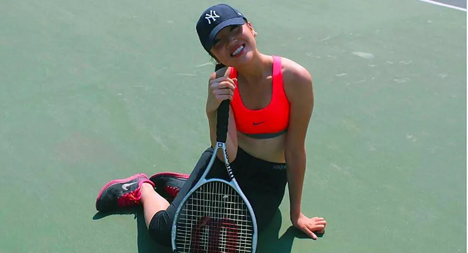 Una persona con una canotta rossa e pantaloncini neri tiene una racchetta da tennis sul campo da tennis del Stephen Leacock Collegiate Institute.