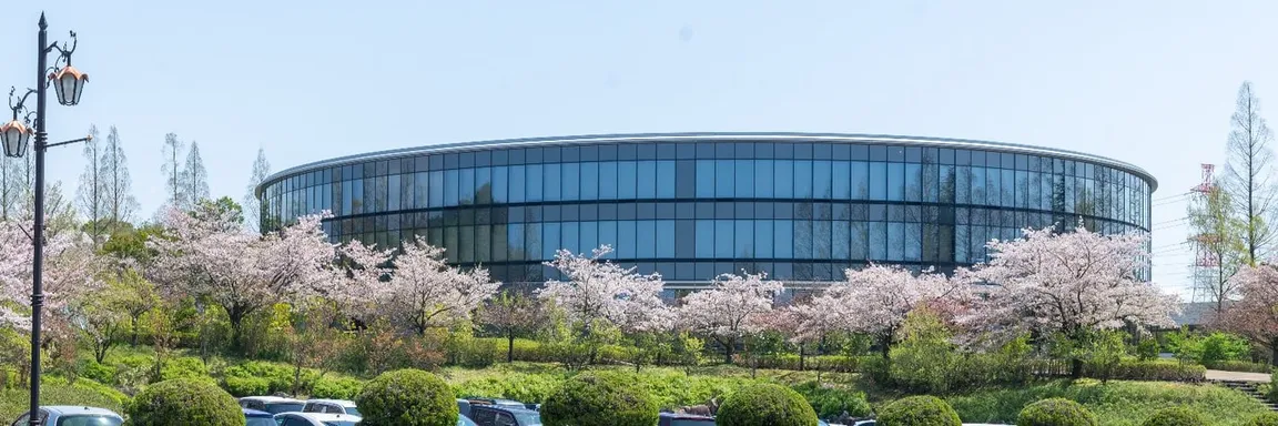 Rundes Glasgebäude eines Campus, umgeben von blühenden Kirschbäumen und Grünflächen