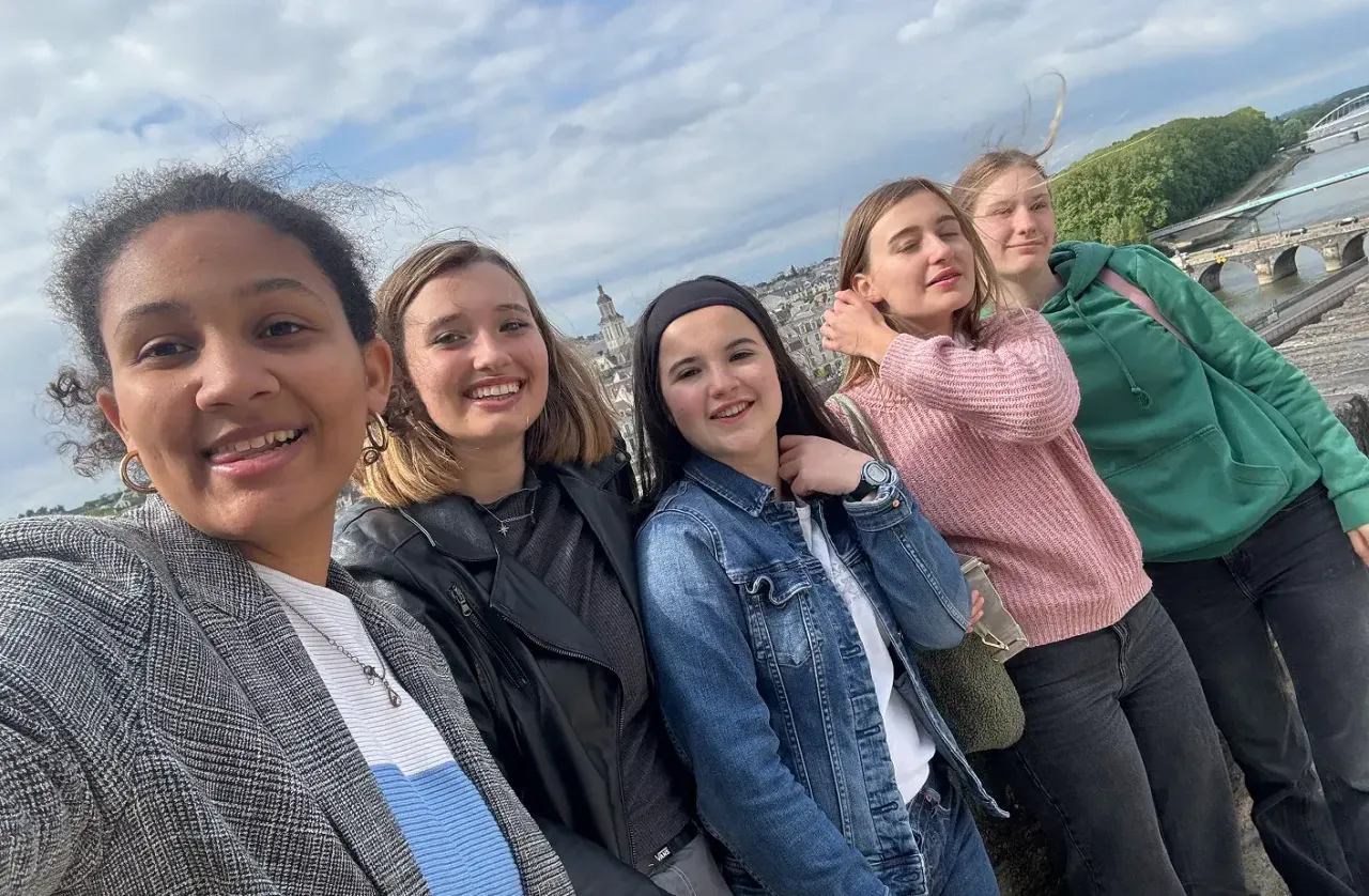 Selfie di cinque studentesse su un muretto con vista su un fiume e una città francese
