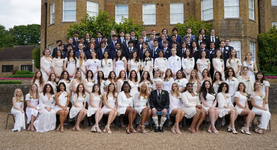 Un gruppo di persone in abito formale in posa davanti a un edificio storico nel campus della TASIS The American International School in England.