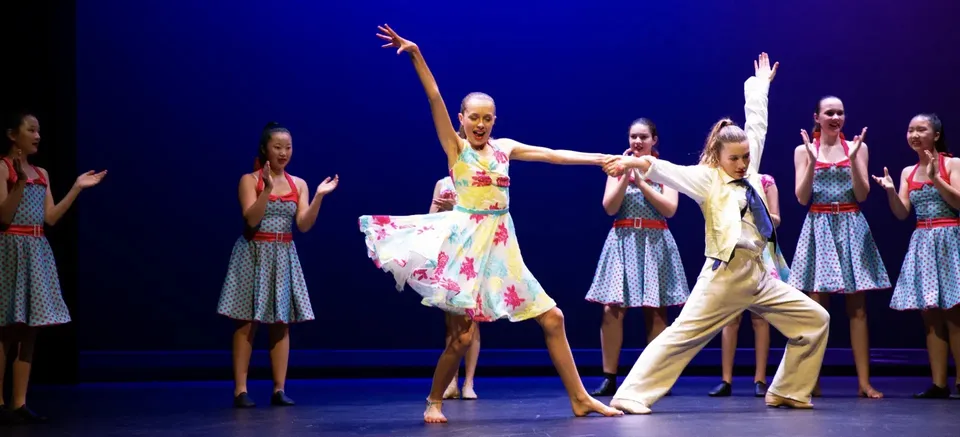 Un gruppo di ballerine si esibisce sul palco della Diocesan School For Girls in uno spettacolo di danza colorato su uno sfondo blu.