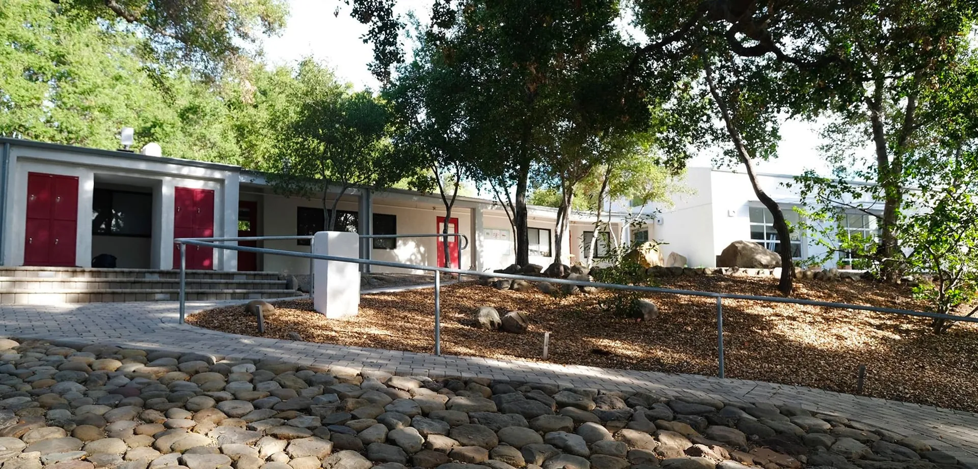 L'edificio scolastico moderno della Besant Hill School è circondato da alberi e mostra un vialetto verso l'ingresso e un giardino roccioso in primo piano.