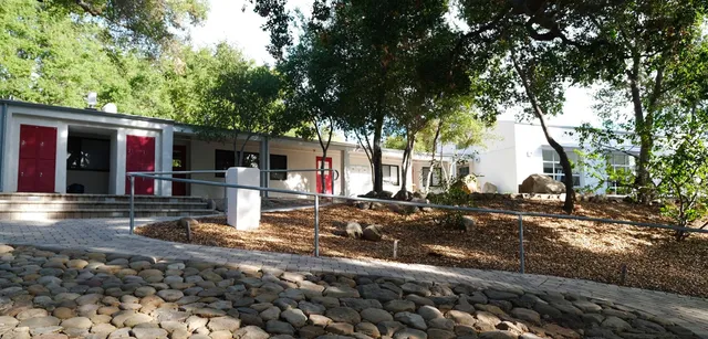 Un edificio bianco della Besant Hill School con porte rosse e un viale pavimentato circondato da alberi.
