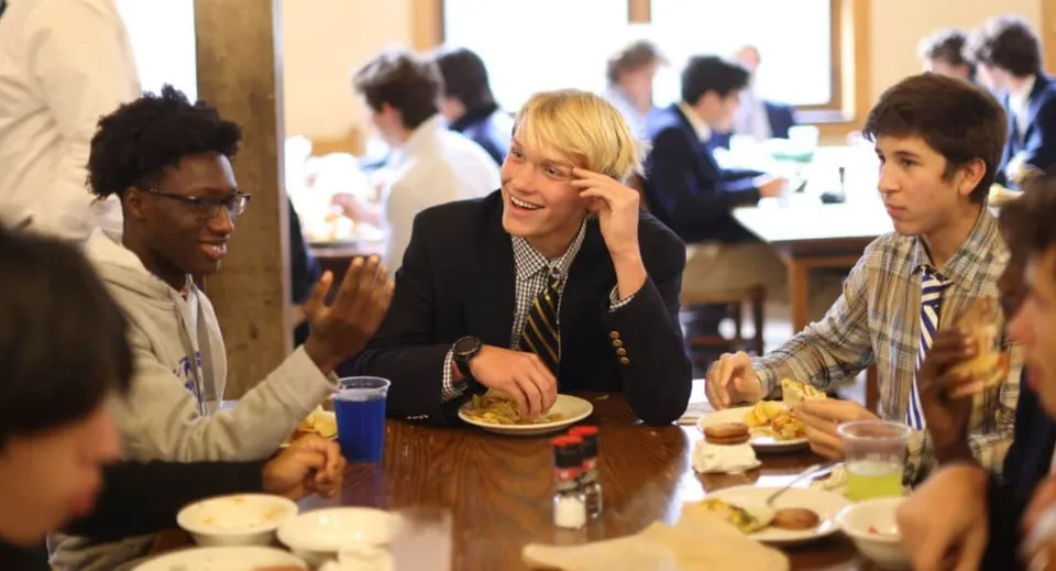 Alcuni studenti della Blue Ridge School sono seduti insieme in una sala da pranzo e chiacchierano mentre condividono un pasto.