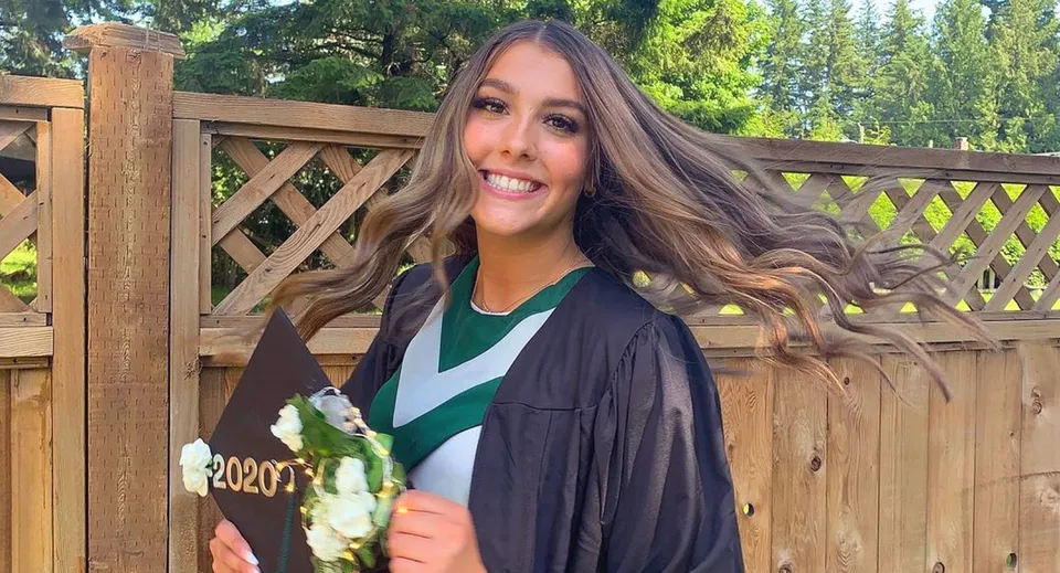 Una studentessa della Robert Bateman Secondary School sorride davanti a una staccionata di legno con molto verde sullo sfondo.