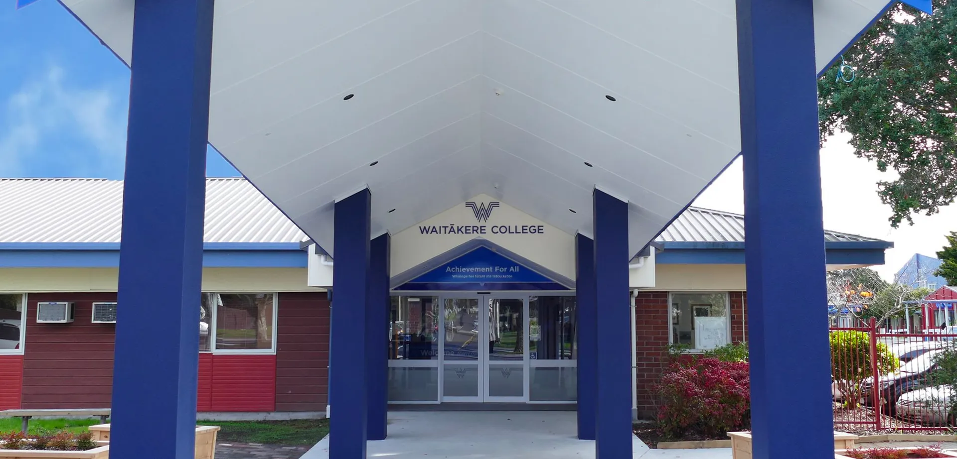 L'edificio moderno del Waitakere College dal design bianco e blu e con porte a vetri è circondato da piante verdi.