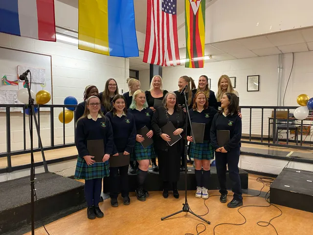 Coro escolar con uniforme posando en el escenario bajo banderas de varios países