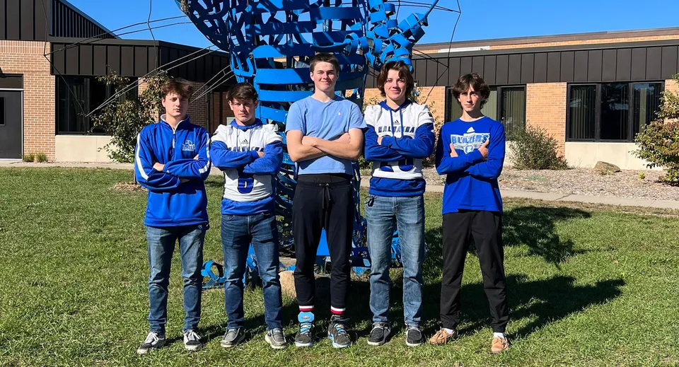 Un gruppo di cinque studenti e studentesse della Kalkaska High School è in piedi davanti a una grande scultura blu e bianca su un prato.
