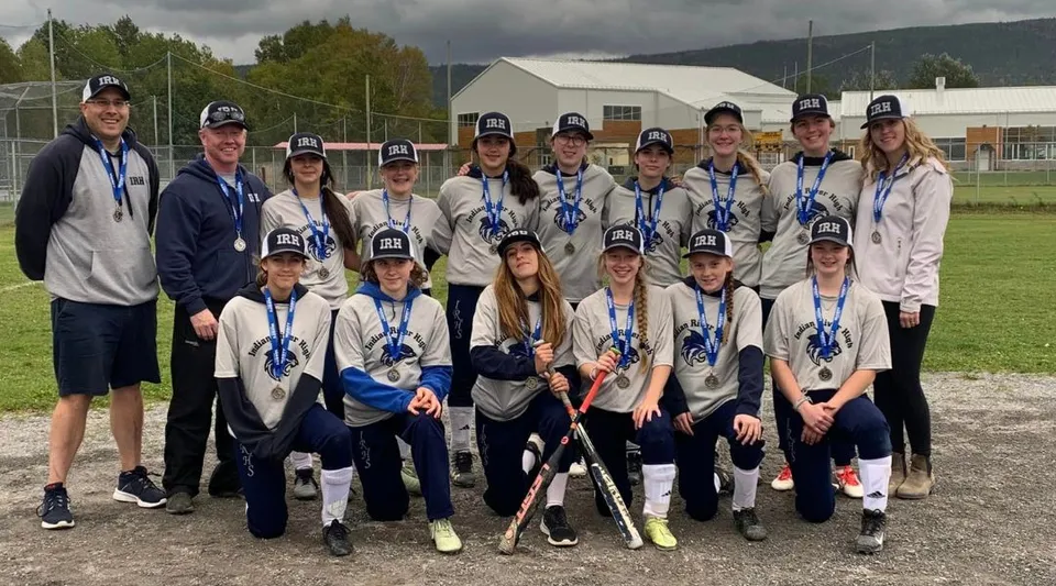 Un gruppo di studenti della Indian River High posa come squadra sportiva all'aperto su un campo davanti a un edificio.