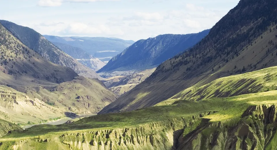 Una valle verde tra le montagne con acqua sullo sfondo nei pressi della Samuel Robertson Secondary School.