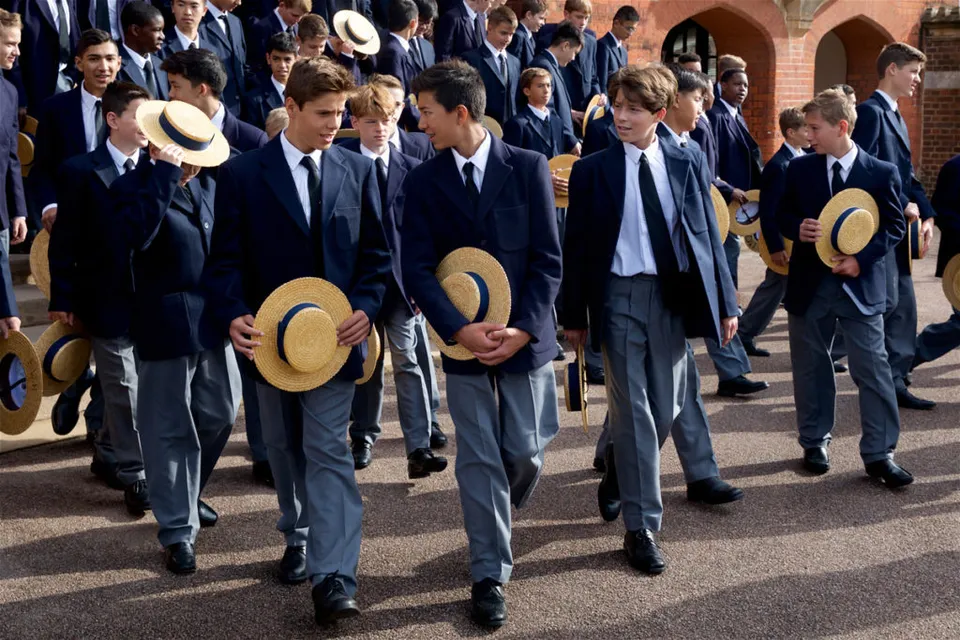 Un gruppo di studenti della Harrow School vestiti in modo formale con abito e cappello passeggia insieme.