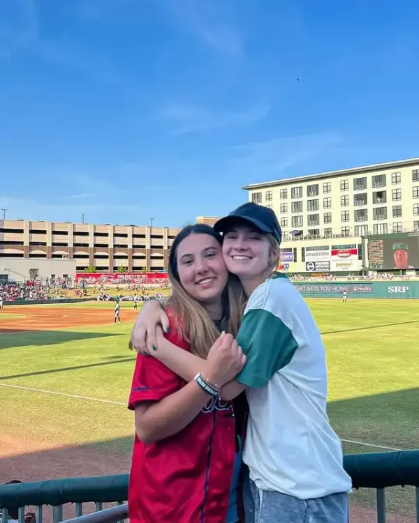 Due ragazze si abbracciano sorridenti in uno stadio da baseball