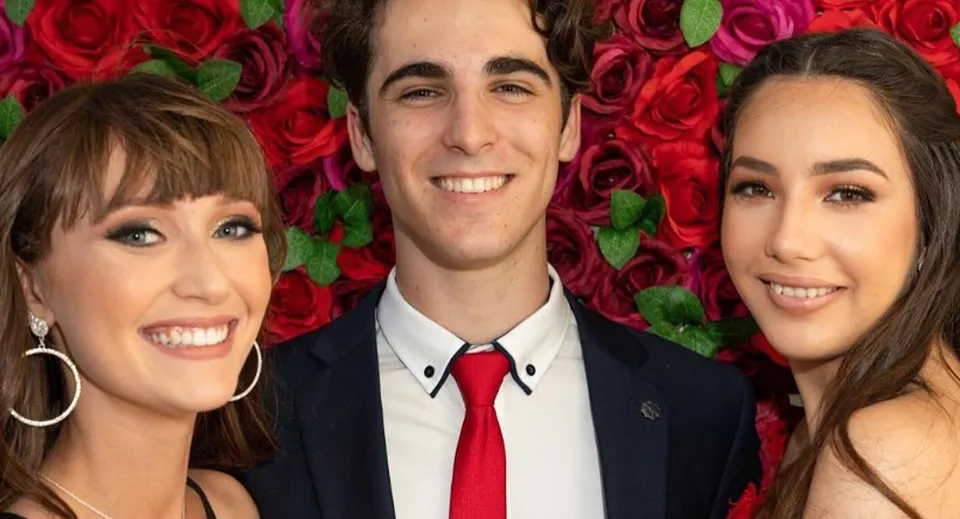 Tre studenti davanti a uno sfondo di rose di un rosso brillante all'interno del campus della Bribie Island State High School.