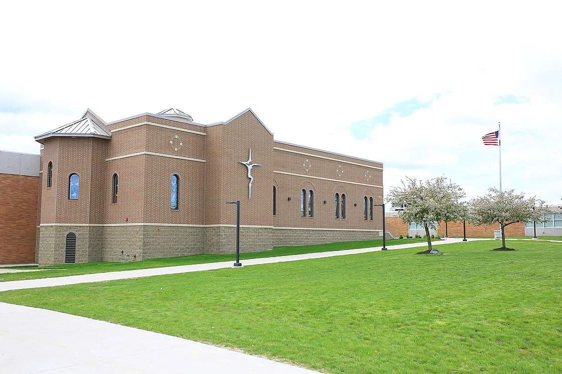 El edificio de ladrillo de la Lansing Catholic High School con una cruz en la fachada y una zona verde en primer plano.