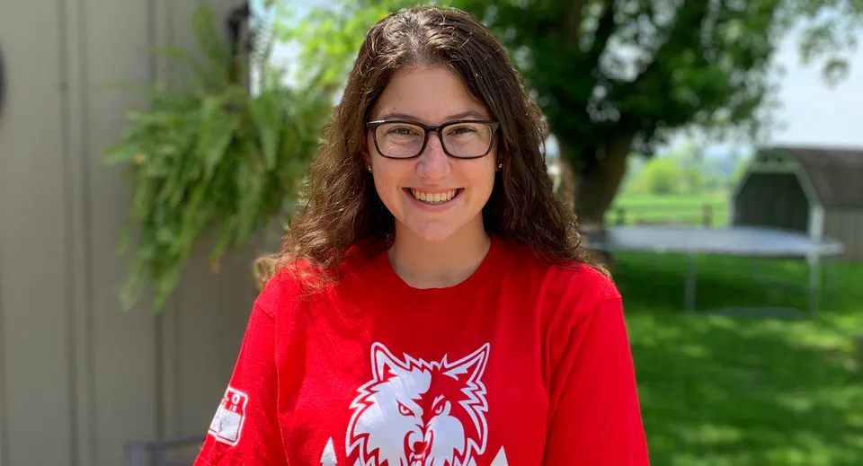 Una studentessa della Nottawasaga Pines Secondary School sorride davanti a un edificio e a uno sfondo di alberi verdi.