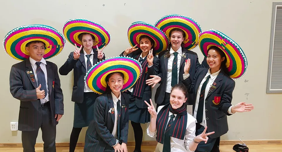 Un gruppo di studenti della Middleton Grange School posa insieme con cappelli e abiti colorati davanti a uno sfondo neutro.