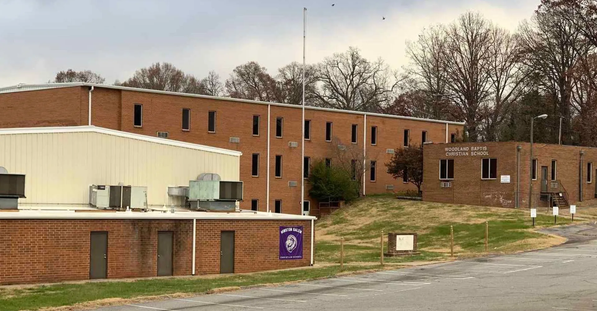 L'edificio in mattoni a più piani della Winston Salem Christian School con l'insegna lilla è circondato da alberi spogli.